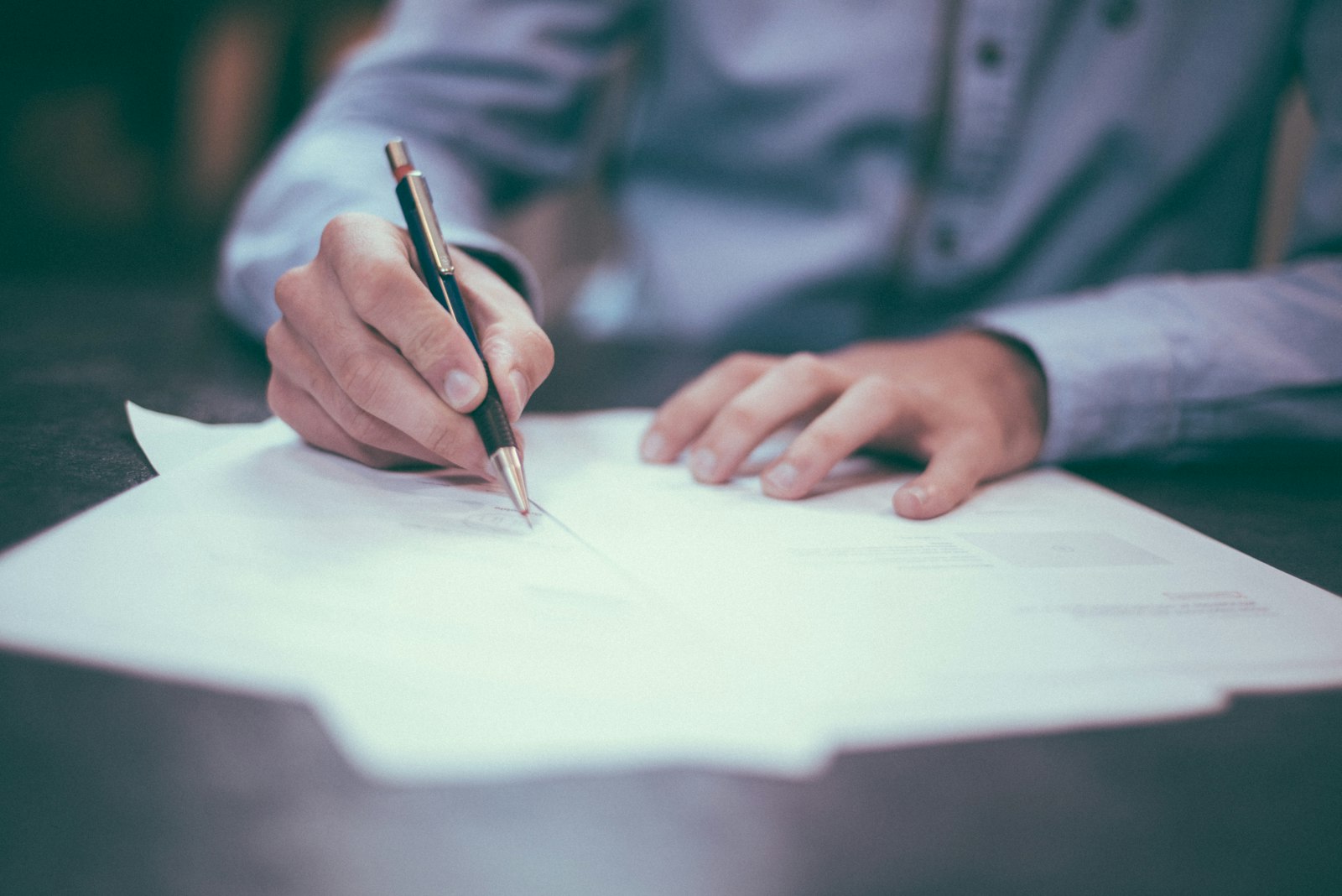 Hands signing closing documents with a pen at a dark table